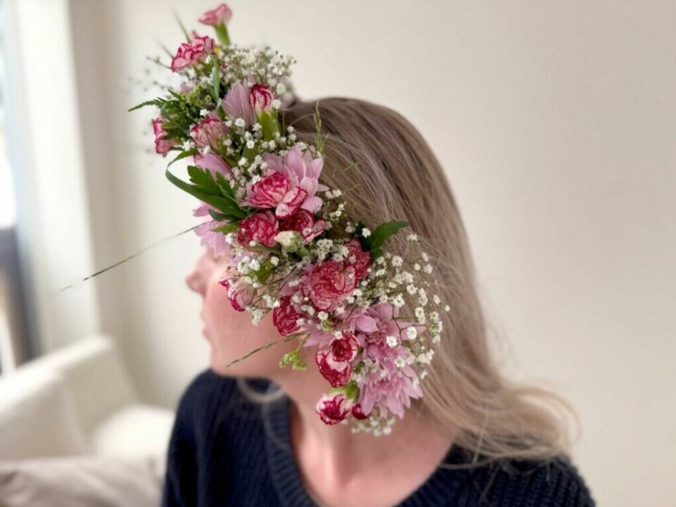 Kransen kan knytes diskret under håret – passer til både løst og oppsatt hår. Blomsterkrans med rosa og røde blomster, sett fra siden på person. Brudeslør og nellik skaper kontraster. Kransen er knyttet under håret.