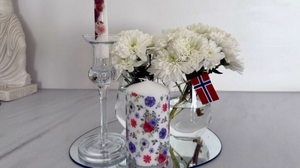 Dette lyset er dekorert med 17. mai-inspirerte servietter og passer perfekt til nasjonaldagens bordpynt. Enkelt å lage med et strykejern og gamle servietter. (Foto: Kreative Ideer/ Aurora Lange) Dekorerte lys med 17. mai-servietter og hvite blomster skaper en elegant og personlig borddekorasjon. Lag dine egne lys med serviett og strykejern – en enkel og miljøvennlig DIY-idé for festbordet.