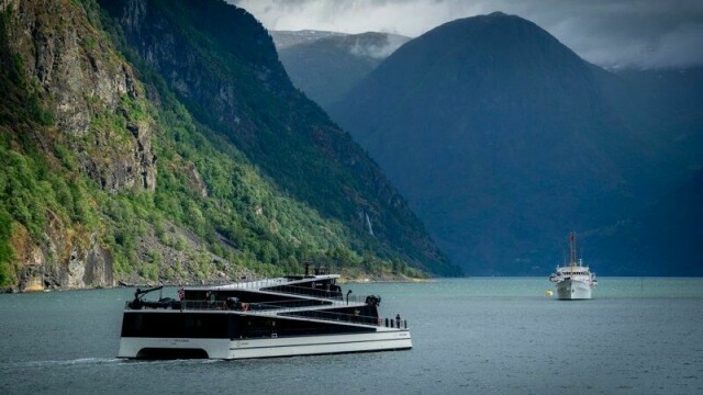 Det er røykutvikling i et batterirom i passasjerkatamaranen Future of the Fjords i Aurlandsfjorden. Skipet går i turistrute mellom Flåm og Gudvangen, her med kongeskipet i bakgrunnen.
