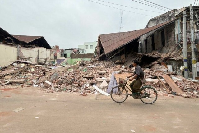 En mann sykler forbi ruinene av en bygning som raste sammen i det kraftig jordskjelvet som rammet Myanmar i slutten av mars. Denne uken ble en astrolog pågrepet for å ha spredd spådommer om et nytt skjelv noen uker etter det første, som krevde flere tusen menneskeliv.