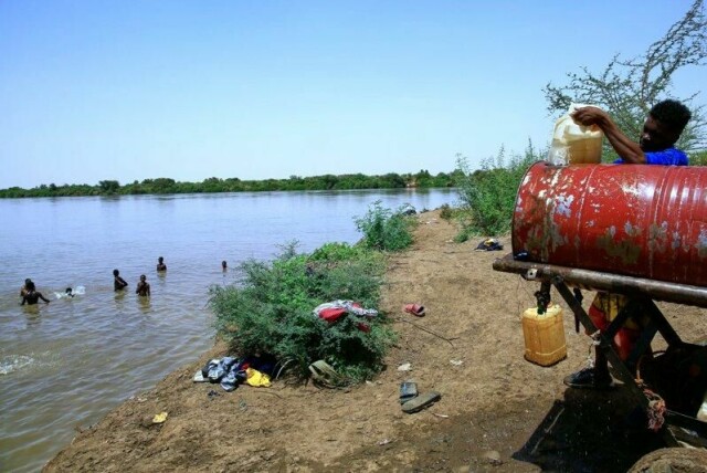 Folk svømmer i Nilen mens en annen fyller opp en vannbeholder som følge av vannstans i Khartoum, hovedstaden i Sudan.