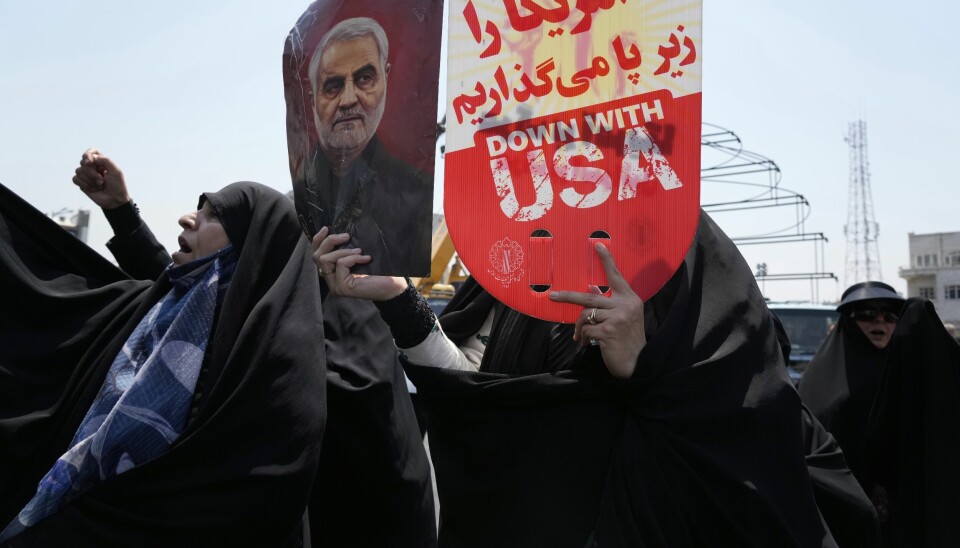En iransk demonstrant viser plakater med antiamerikanske budskap og et bilde av den likviderte iranske generalen Qasem Soleimani, som ble drept i et amerikansk angrep i Irak i 2020, i Teheran fredag. USAs president Donald Trump roser Israels angrep i Iran natt til fredag.