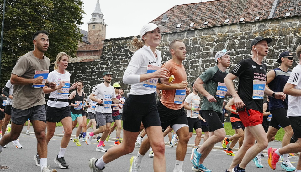 Oslo maraton ble utsolgt på rekordtid i 2025, og var ifølge NRL «skrapet for billetter allerede i mars». Bildet viser en gruppe maratonløpere i aksjon under Oslo Maraton. Akershus festning er tydelig synlig i bakgrunnen. Deltakerne løper i jevnt tempo, mange med fokuserte eller smilende ansiktsuttrykk. De bærer startnummer med blå og hvite farger, og noen har navnelapper. Løperne er kledd i teknisk treningstøy og joggesko i ulike farger, og noen har på seg caps, solbriller eller ørepropper. Stemningen er energisk og preget av konsentrasjon, typisk for en mellomfase i et løp. Festningens gamle steinmur og tårn gir en tydelig kontrast til den moderne og dynamiske aktiviteten.