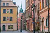 Dette bildet viser en sjarmerende gate i gamlebyen i Warszawa, Polen. Gaten er omgitt av historiske bygninger med fasader i varme farger som gult, oransje og rosa. På den ene bygningen ser vi fargerike veggmalerier, mens en annen bygning har et skilt for et kunstgalleri. I bakgrunnen troner en bygning med et klokketårn, sannsynligvis den kongelige slottet i Warszawa, som har en karakteristisk grønn kuppel og et klokketårn. Gaten er brosteinsbelagt og har klassiske gatelykter som gir en følelse av historisk sjarm og europeisk kulturarv. Vi gir deg tips til hva du kan se og gjøre i storbyen Warszawa. Blant annet Stare Miasto (Gamlebyen), Krakowskie Przedmieście, Łazienki-parken, Nowy Świat-gaten og Wilanów-palasset. Byen er perfekt for en storby-weekend i Europa.