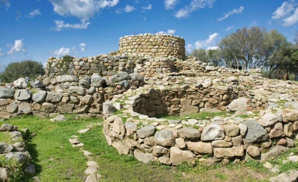 Hvis du er interessert i historie kan Sardinia blant annet by på Nuraghe-ruinene som står på UNESCOs verdensarvliste. (Foto: Colourbox) Et bilde av Nuraghe-ruinene på Sardinia, Italia, som viser gamle steinstrukturer bygget av store, steinblokker. Den mest fremtredende strukturen er et rundt tårn som er delvis intakt, omgitt av lavere murfragmenter og sirkulære steinformasjoner. Området rundt er dekket av grønt gress og ville blomster, og det er trær i bakgrunnen mot en blå himmel med spredte skyer. Middelhavsøya Sardinia byr på både luksus og spennende historie, og her finner du krystallklar sjø og kritthvite strender. Vi gir deg tips til hva du kan se og gjøre på den italienske øya i Middelhavet; Dra til Smaragdkysten, Grotta di Nettuno, Nuraghe-ruinene, La Maddalena-øygruppen. Vi hjelper også med å finne hotell på Sardinia.