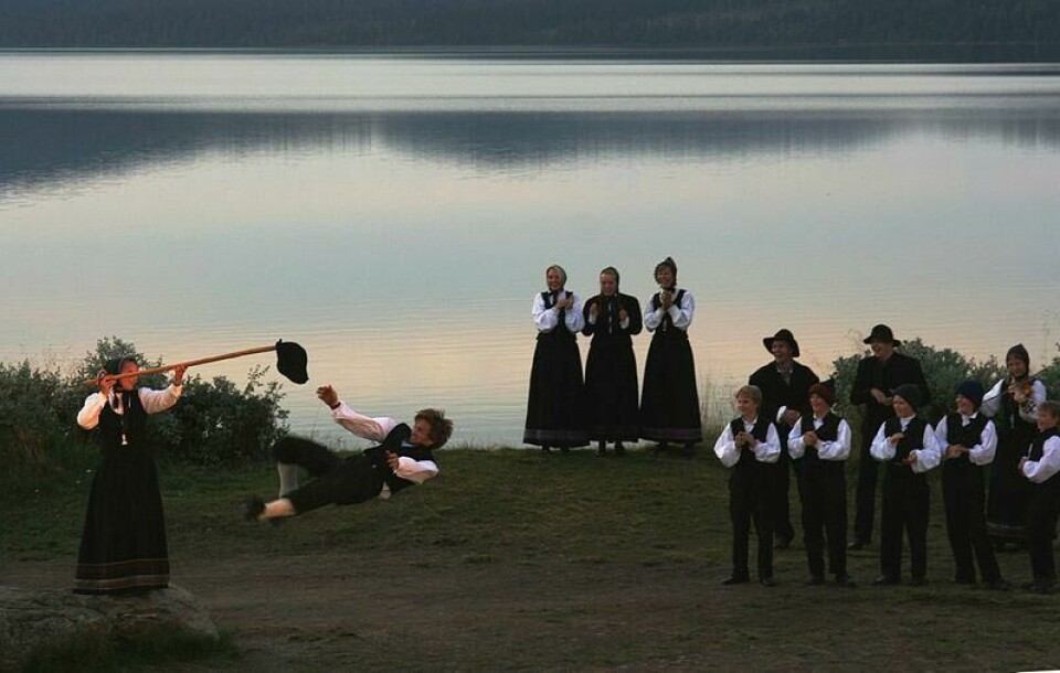 Halingsparket er den store manndomsprøven for menn i bunad på 17. mai. Dette er også morsomt for barna. (Foto: Marcus Ramberg / SNL / CC.BY.2.0)) Bilde av voksne som danser og leker hallingkast og hallingdans i solnedgang. Ikledd bunader og ved et blikkstille vann. Vi tipser om 17 morsomme 17. mai-leker for voksne og barn.