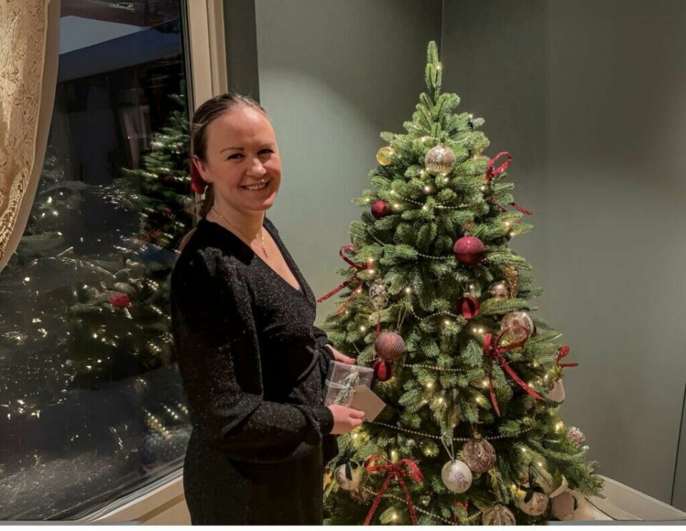 Anette Christoffersen står ved siden av et pyntet juletre med smil og holder en julegave i hånden, klar for å feire jul. (Foto: Kreative ideer/ Aurora Lange)