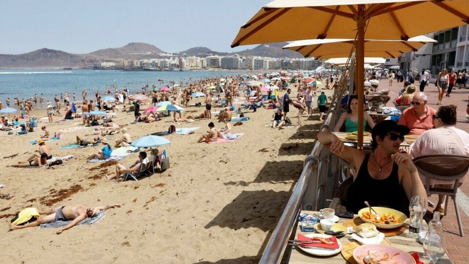 Gran Canaria tiltrekker seg turister fra hele verden. Men nå kommer turistskatten til Puerto Rico, Arguineguín, Puerto de Mogán og Mogán (Foto: Lise Åserud/ NTB) Bildet viser en solrik strand på Gran Canaria, full av turister som nyter det varme været. I forgrunnen sitter flere personer ved et bord på en restaurant med parasoller, mens de spiser og slapper av. Bak dem er stranden full av solbadere og parasoller, med noen som ligger på sanden og andre som står og går. Langs stranden sees moderne bygninger og fjell i bakgrunnen, som setter den vakre kysten i kontrast.