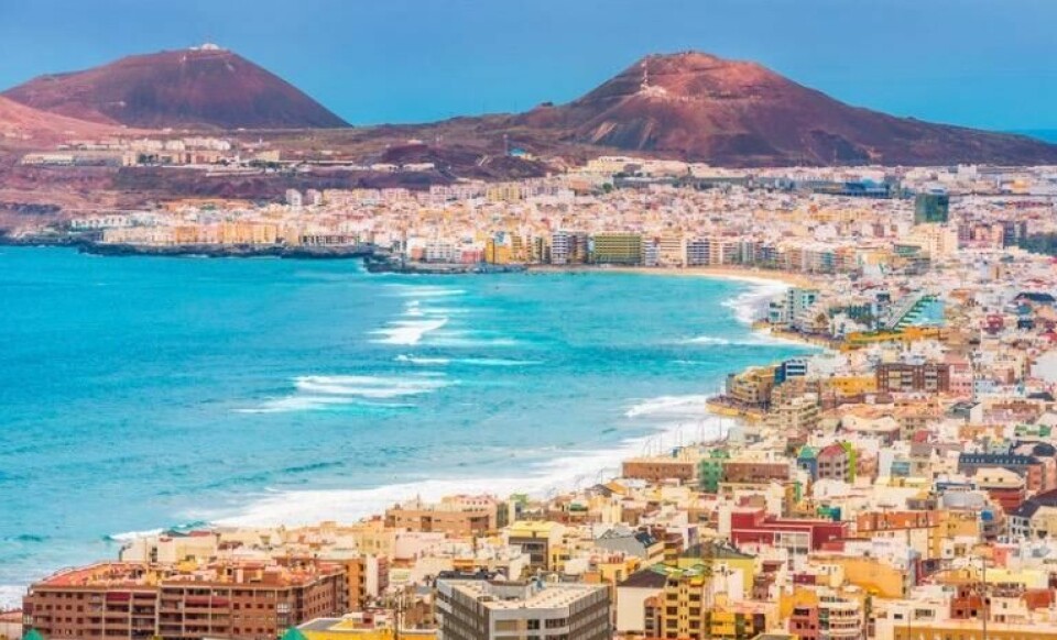Las Palmas kombinerer by og strand på en sømløs og fantastisk måte (Foto: Canva) Bildet viser en vakker kystby ved havet, trolig Las Palmas på Gran Canaria. Forgrunnen er fylt med bygninger i ulike farger og arkitektoniske stiler. Langs vannkanten kan man se en strand som strekker seg langs byen. Havet er klart og blått, med bølger som ruller inn mot land. I bakgrunnen er det fjell, som gir en dramatisk kontrast til kystlandskapet. Stemningen er livlig og typisk for et solfylt, turistvennlig sted ved Atlanterhavet. kanariøyene er en stor favoritt blant rensende nordmen og mange legger vinterfeien, juleferie og høstferie hit.