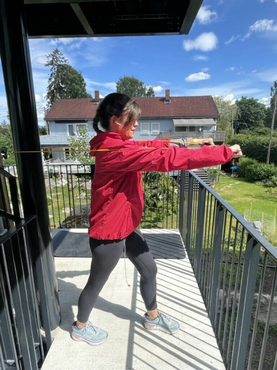 Brystpress med treningsstrikk er en effektiv øvelse for bryst og fremside av skuldre. (Foto: Cecilie Aasland / ABC Startsiden) Bilde av en dame i rosa treningsjakke, svarte tights og blå løpesko fra Hoka, som gjennomfører et treningsprogram for hjemmetrening som trener styrke for hele kroppen med treningsstrikker. Hun står ute i en oppgang med en treningsmatte og i bakgrunnen er det grå rekkehus, frodig grønn plen og trær. På bildet trener hun brystpress med treningsstrikk, en effektiv øvelse for bryst og fremside av skuldre.