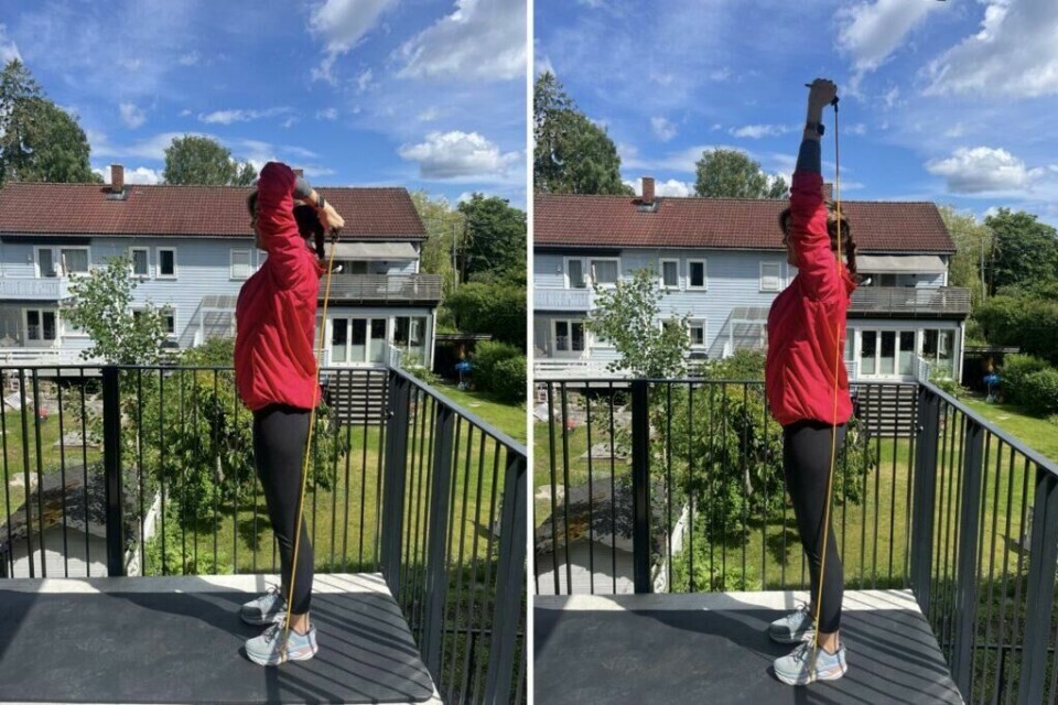 Ved stående tricepspress med treningsstrikk trener du både triceps og bakside overarm! (Foto: Cecilie Aasland / ABC Startsiden) Bilde av en dame i rosa treningsjakke, svarte tights og blå løpesko fra Hoka, som gjennomfører et treningsprogram med hjemmetrening som trener styrke for hele kroppen med treningsstrikker. Hun står ute i en oppgang med en treningsmatte og i bakgrunnen er det grå rekkehus, frodig grønn plen og trær. På bildet trener hun stående tricepspress med treningsstrikk og her trener hun både triceps og bakside overarm!