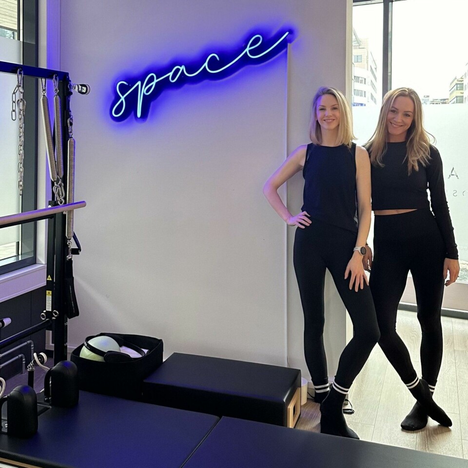 Vi skapte SPACE for å kunne ta med oss vår favoritt måte å trene på fra London til Oslo, sier grunnleggere av SPACE Pilates Oslo, Kristina Cavanna og Aislinn Jensen. (Foto: SPACE Pilates ) Bildet viser to kvinner kledd i svart treningstøy som står inne i et moderne pilatesstudio. De smiler og poserer selvsikkert foran en reformer-maskin, som er et populært treningsapparat innen pilates. På veggen bak dem lyser et blått neonskilt med ordet 'space', som ser ut til å være navnet på studioet. Studioet har store vinduer som slipper inn naturlig lys, og i bakgrunnen kan man se bygninger utenfor. Atmosfæren virker moderne, innbydende og profesjonell, med en minimalistisk innredning og rene linjer. Vi skapte SPACE for å kunne ta med oss vår favoritt måte å trene på fra London til Oslo, sier grunnleggere av SPACE Pilates Oslo, Kristina Cavanna og Aislinn Jensen.