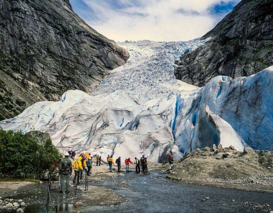 Opplev Briksdalsbreen på norgesferien din til Gamle Strynefjellsvegen. (Foto: Jarle Waehler/Statens vegvesen) En gruppe turgåere med fargerike klær og turstaver nærmer seg en stor isbre som strekker seg oppover fjellsiden. Isbreen er blåhvit og sprekker opp i store isblokker. Området rundt isbreen er preget av steinete terreng og bratte klipper. Himmelen er delvis skyet, og fjellene rundt gir et majestetisk og dramatisk landskap. Her får du tips til syv vakre bilturer i Norge som er perfekt for norgesferien. Geiranger og Trollfjorden, Atlanterhavsveien, Lofoten, Hardanger, Rondane, Gamle Strynefjellsvegen, Senja.