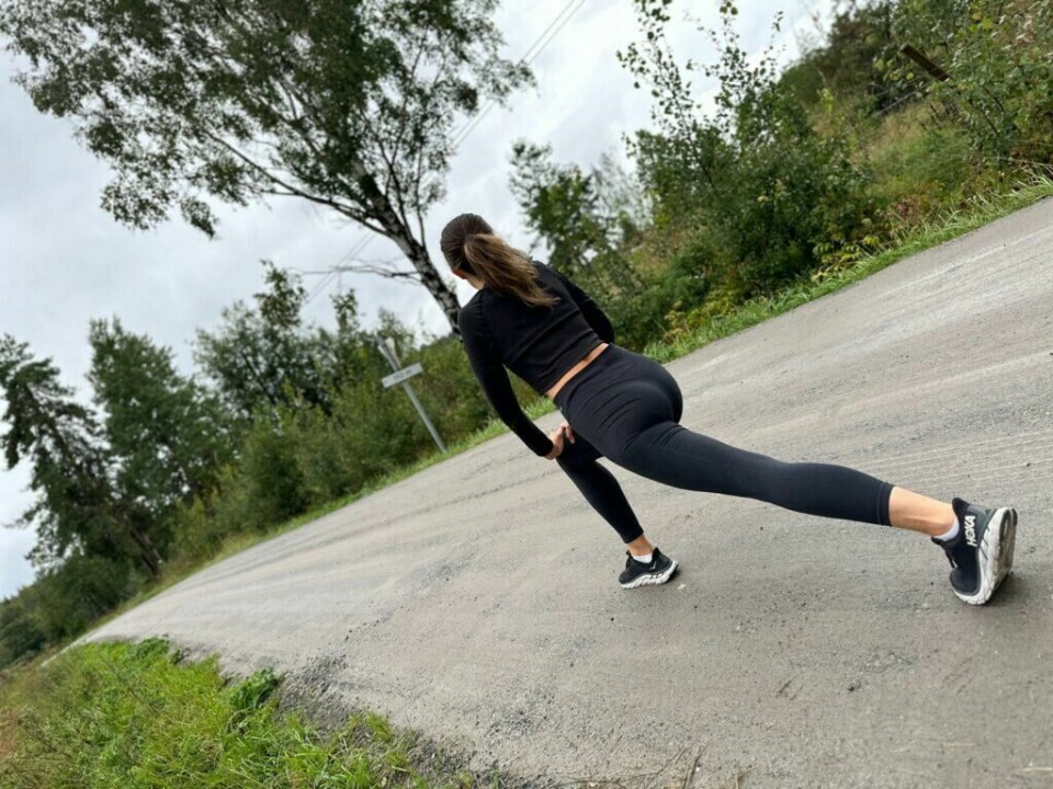 Anbefalingen er å ikke gjøre øvelser om du ikke kan gjøre de riktig når du har gangsperre, men heller ikke å la være å trene fordi at du er støl, for da kan plagene bli verre. (Foto: Mari-Ann Greiner Green) Bildet viser en kvinne som gjør en dyp utfallsøvelse på en grusvei. Hun er kledd i mørk treningstøy, med sorte joggesko og en langermet topp. Kvinnen er plassert med ryggen til kameraet, og posisjonen hennes viser en kraftig strekk i bakbenet mens hun støtter seg på det fremre benet. Vegetasjon og trær omgir veien, og himmelen er overskyet, noe som gir en frisk og naturlig atmosfære. Øvelsen ser ut til å være en del av en oppvarming eller nedtrapping etter fysisk aktivitet. Vi forklarer hva stølhet skyldes, hva som hjelper mot og hvordan man kan kvitte seg med stølhet og gangsperre og ikke minst om det anbefales at man trener når man er støl eller har gangsperre?