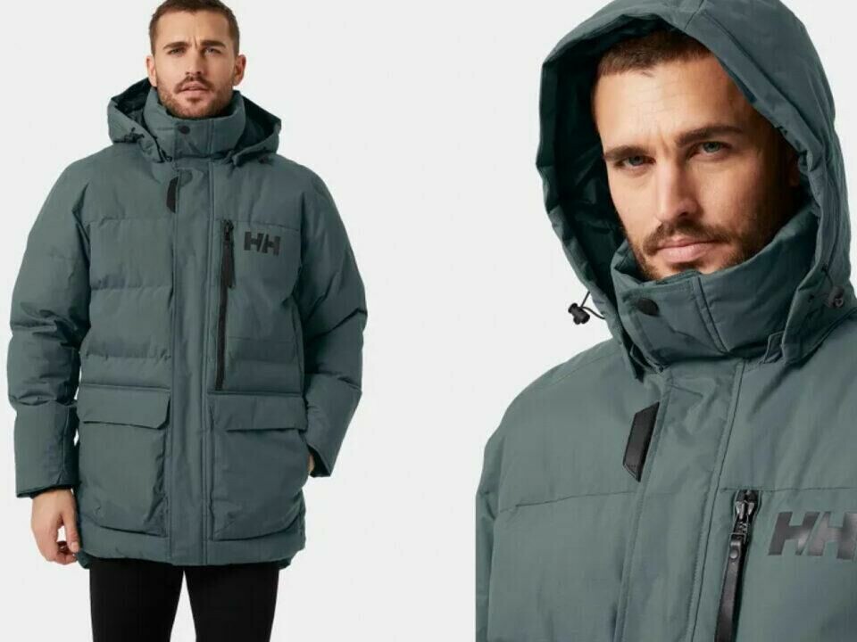 Tromsø vinterjakke fra Helly Hansen, sørger den for at du holder deg god og varm på de kaldeste dagene! (Foto: Helly Hansen) Bildet viser en mann iført en grå Helly Hansen-vinterjakke. Jakken har en tykk, isolerende polstring og er designet for å tåle kaldt vær. Den har en høy krage og en justerbar hette for ekstra beskyttelse mot vind og kulde. På brystet til venstre er Helly Hansen-logoen (HH) synlig. Jakken har store lommer foran for både oppbevaring og varme til hendene, samt en brystlomme med glidelås. Designet er funksjonelt og stilrent, med en noe lengre passform som gir god dekning og beskyttelse mot elementene.