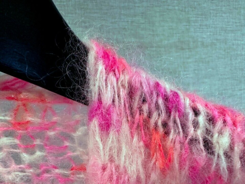 Fargerik silk mohair-jakke som slipper løse fibre – slik kan du redusere røyting av ullplagg. (Foto: Kreative Ideer/ Miriam Schjetlein) Bildet viser en strikket jakke laget av silk mohair-garn, kjent for sin luftige og myke tekstur, men også for å slippe løse fibre. Jakken har en fargerik blanding av rosa, lilla og kremhvit, med tydelige, bustete ulltråder som stikker ut. Den er drapert over en sort kleshenger, som skaper en kontrast mot de myke fibrene. Bakgrunnen er nøytral, noe som lar teksturen og fargene i garnet stå frem. Dette bildet illustrerer hvordan slike ullplagg kan røyte, spesielt når de er laget av mohair, og kan brukes i en artikkel om metoder for å minimere røyting.