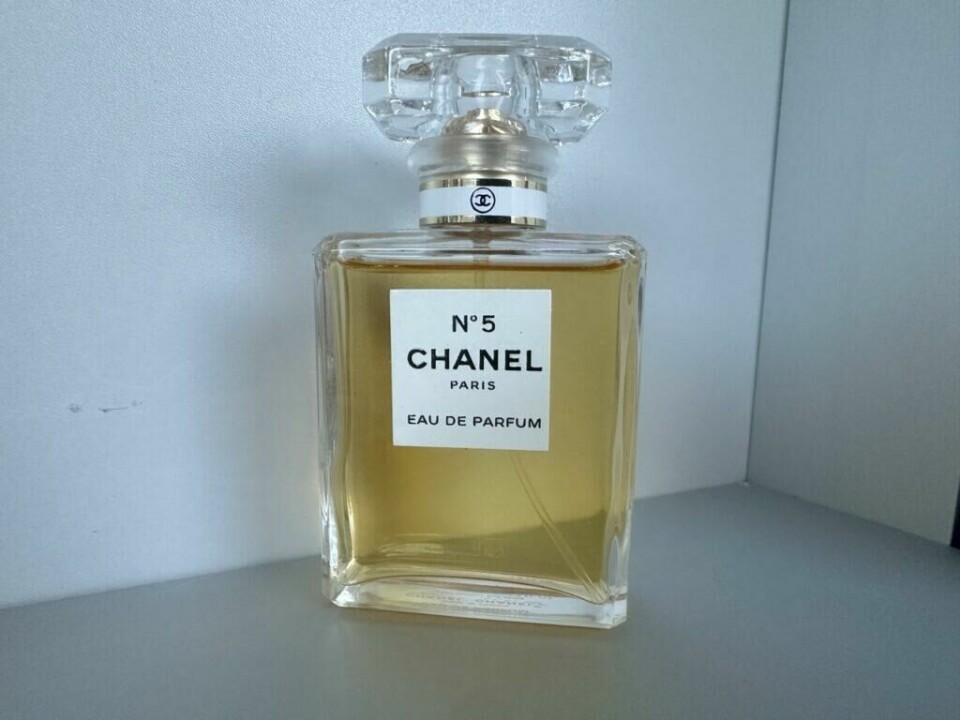 En ikonisk flaske med Chanel No. 5 Eau de Parfum, et tidløst symbol på eleganse og luksus. (Foto: Kreative Ideer/ Aurora Lange) En klar glassflaske med den velkjente parfymen Chanel No. 5. Flasken har et minimalistisk design med en firkantet form, fylt med en gylden væske. På etiketten står det 'CHANEL No. 5 Paris Eau de Parfum.' Flasken står plassert mot en enkel, lys bakgrunn som fremhever dens klassiske og stilrene utseende.