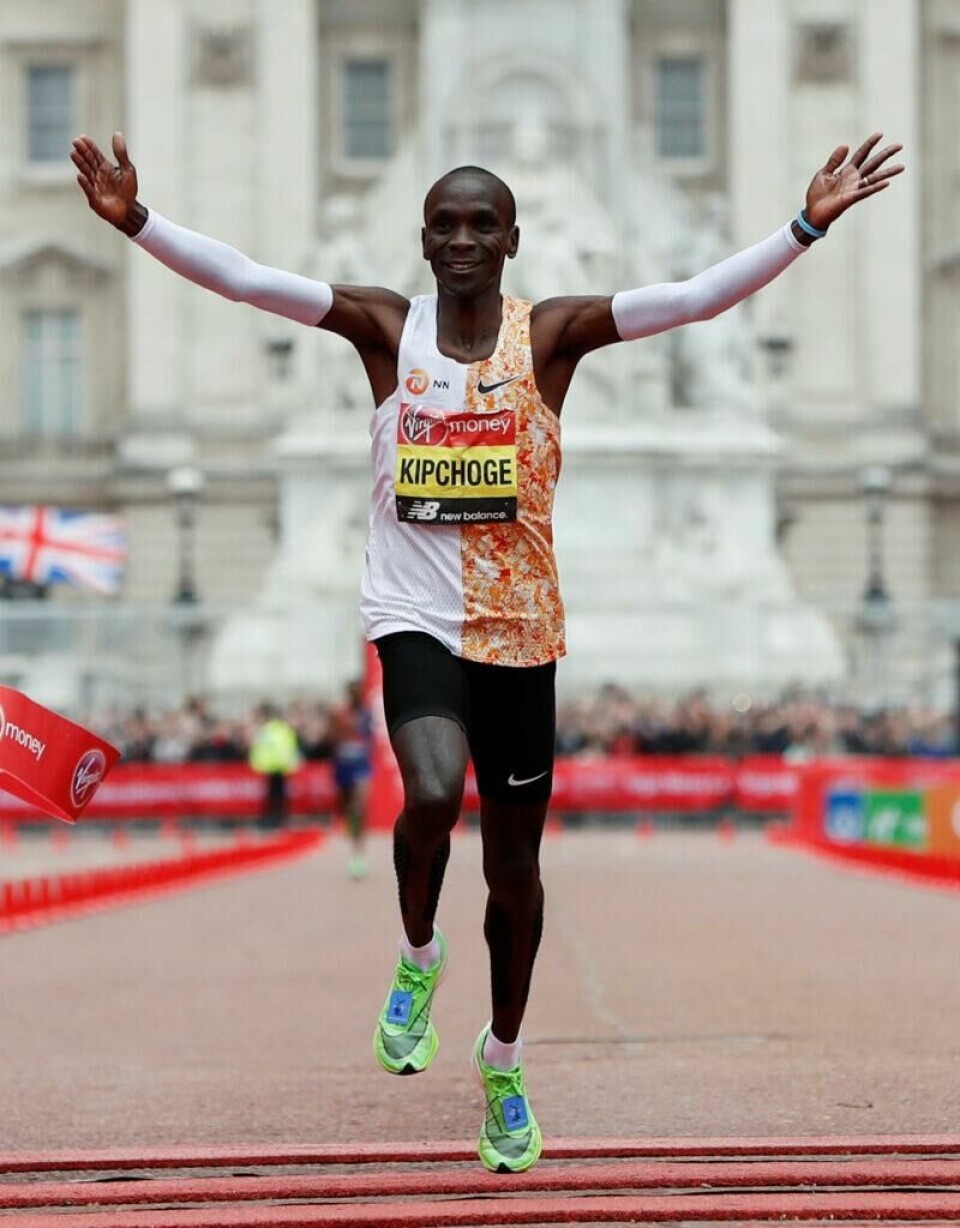 Eliud Kipchoge, for mange kjent som mannen med verdens raskeste, uoffisielle maraton-rekord, er kjent for å bevist benytte seg av ansiktsmimikk for å roe seg ned og holde ut når han løper. Bildet viser den kenyanske maratonløperen Eliud Kipchoge i det han krysser målstreken under London Marathon. Han er kledd i en løpetrøye med en halvt oransje og hvit design, sorte løpeshorts og lysegrønne løpesko. Kipchoge har armene løftet i triumf og smiler bredt, tydelig fornøyd med prestasjonen. I bakgrunnen er det en stor, staselig bygning og flere tilskuere som heier. Bildet fanger øyeblikket av seier og glede etter en imponerende prestasjon i maratonløpet, og illustrerer hvordan et smil kan være en naturlig reaksjon på suksess under trening og konkurranse. Eliud Kipchoge, for mange kjent som mannen med verdens raskeste, uoffisielle maraton-rekord, er kjent for å bevist benytte seg av ansiktsmimikk for å roe seg ned og holde ut når han løper.
