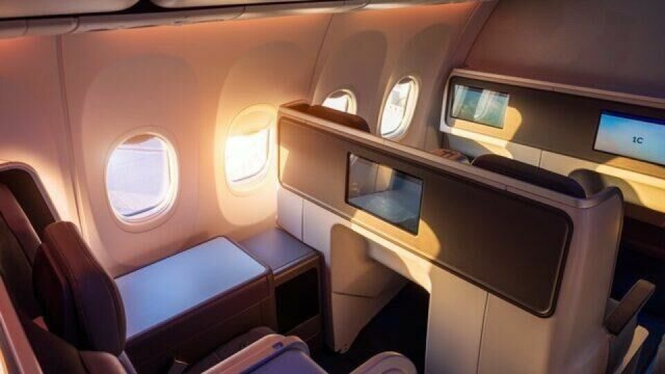 Et luksuriøst businessklasse-sete ombord på et moderne fly, med privat skjerming, individuell TV-skjerm og et innbydende sollys som strømmer inn gjennom vinduene.