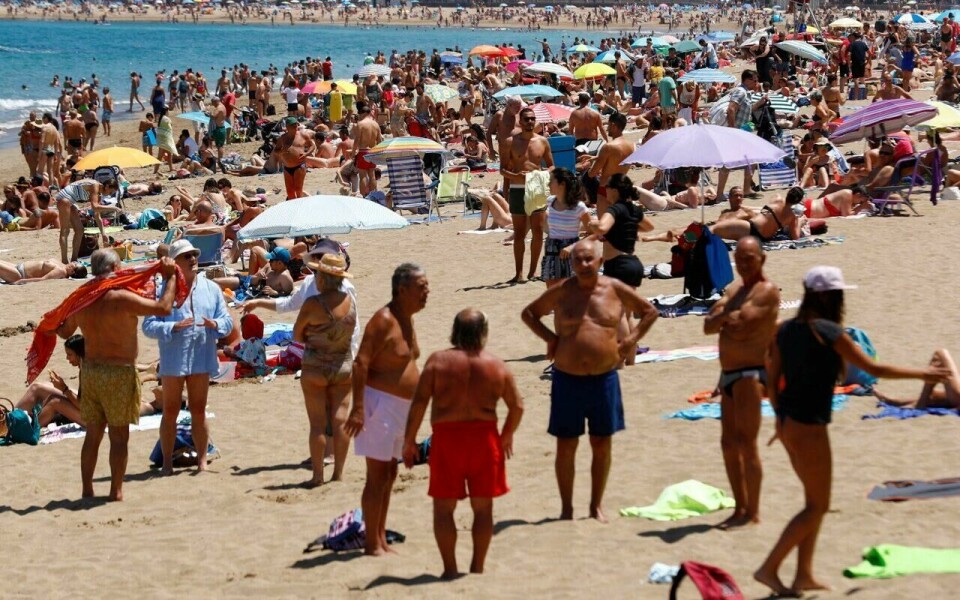 Nye varmerekorder på Kanariøyene (Foto: Reuters) Bildet viser en travel sandstrand full av mennesker som nyter sol og varme. Stranden er tettpakket med solsenger, parasoller og strandutstyr. Mange mennesker står eller sitter i små grupper, mens andre ligger på håndklær og soler seg. Havet i bakgrunnen er blått, og vi kan se flere mennesker som bader. Langs kystlinjen skimtes bygninger, noe som tyder på at dette er en strand nær en by eller et populært turistområde, sannsynligvis et sted som Gran Canaria. Atmosfæren er livlig, og det ser ut til å være en varm og solrik dag.