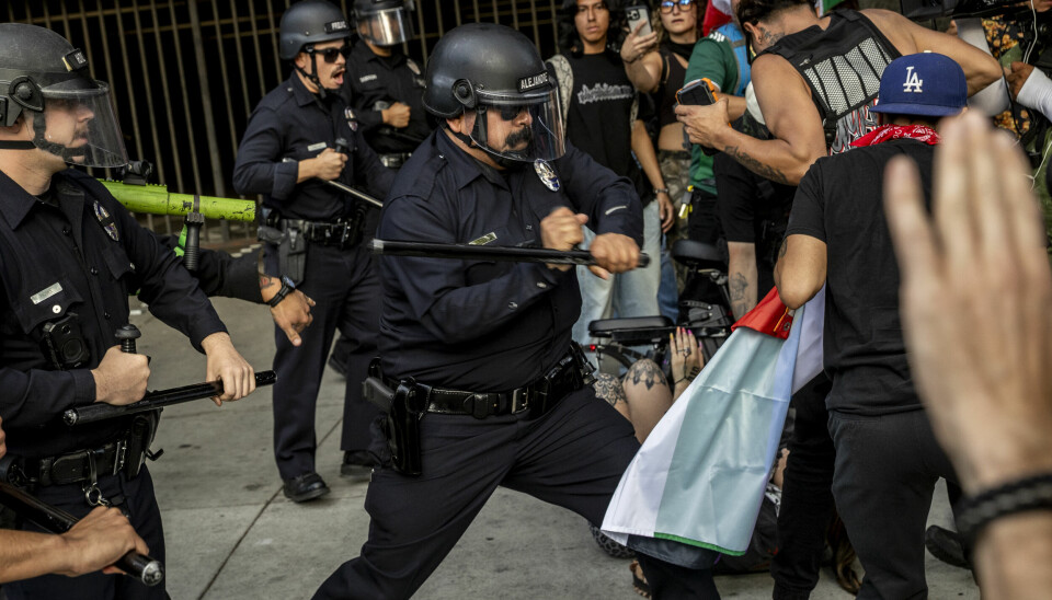 En politibetjent bruker batong mot en person under en demonstrasjon i Los Angeles. Bildet er tatt lørdag 14. juni.