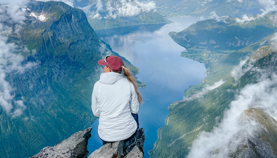 Alternative fjellturer i Norge: – Jeg ble blåst av banen En kvinne med rød caps og hvit jakke sitter helt ytterst på en fjellkant og ser ut over et dramatisk landskap. Under henne slynger en dyp fjord seg mellom bratte fjellsider, med små bygder langs vannkanten. Skyene driver rundt tindene, og utsikten er luftig og overveldende. Dette er fjelltur på sitt mest spektakulære – et øyeblikk fra en tur gjennom Slogenrunda eller en annen krevende rundtur i Sunnmørsalpene.
