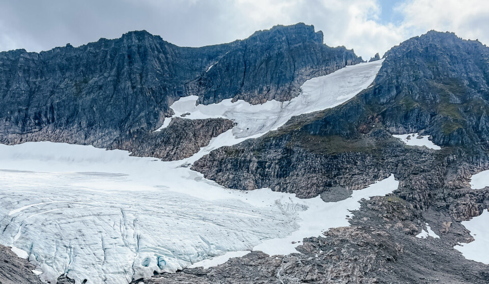 Et turkisblått brevann ligger stille nedenfor en mektig isbre som bukter seg ned fra fjellsiden. Rundt vannet ruver bratte og taggete fjelltopper, noen med snøflekker langt nedover fjellet. Landskapet er nakent og dramatisk – typisk for høyfjellet i Sunnmørsalpene. Dette motivet kan oppleves langs Slogenrunda, en rundtur som tar deg tett på isbreer og stupbratte tinder i hjertet av Sunnmøre.