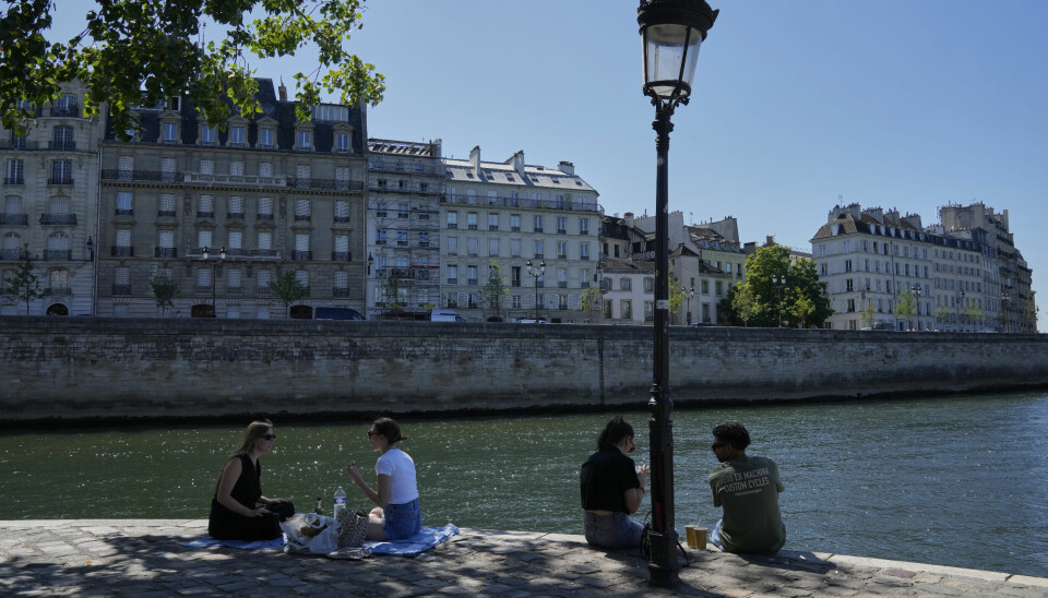 Folk sitter i skyggen langs Seinen i Paris.