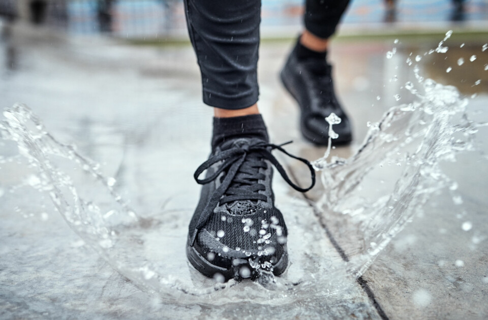 Vanntette joggesko som tåler regnvær? Vi har samlet de beste modellene ifølge pålitelige tester i 2025. Nærbilde av svarte joggesko som tråkker i en vannpytt. Vannsplash rundt skoen illustrerer vanntetthet. Artikkelen omtaler de beste vanntette joggeskoene i 2025 basert på eksterne tester.
