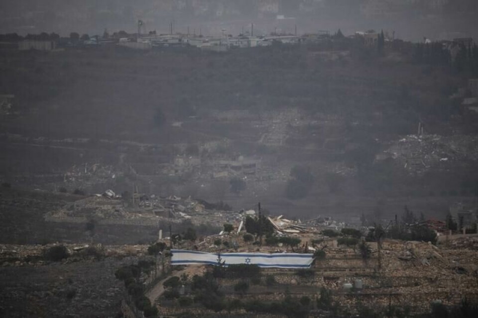 Israelske soldater har rullet ut et stort israelsk flagg ved siden av bombede hus i Sør-Libanon. I bakgrunnen ligger en av basene til FNs fredsbevarende Unifil-styrke. Israelske soldater har rullet ut et stort israelsk flagg ved siden av bombede hus i Sør-Libanon. I bakgrunnen ligger en av basene til FNs fredsbevarende Unifil-styrke. Foto: AP / NTB