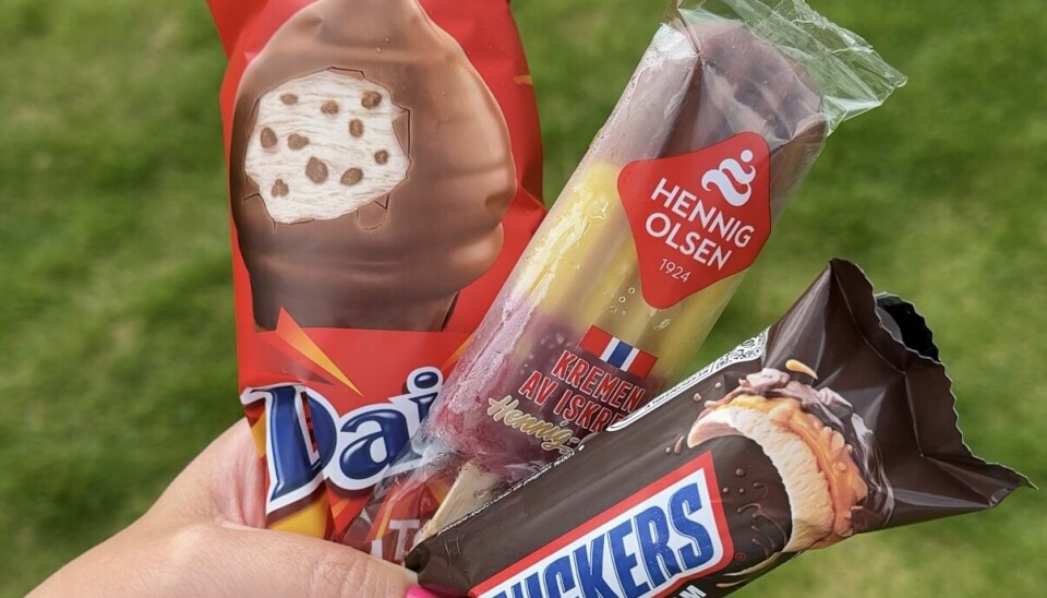 Tre favoritter fra iskremdisken Nærbilde av en hånd som holder tre ulike iskremer utendørs på en sommerdag med grønt gress i bakgrunnen. Produktene inkluderer Daim Balltop fra Freia/Hennig-Olsen, en klassisk flerfarget pinneis fra Hennig Olsen med teksten 'Kremen av iskrem', og Snickers Ice Cream bar – en kombinasjon av sjokolade, karamell og peanøttis. Bildet viser populære isvalg i Norge, perfekt for varme sommerdager og utendørs kos.