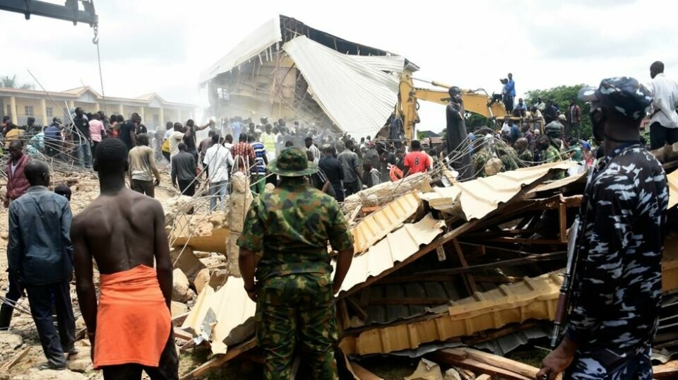 Folk samlet seg utenfor den sammenraste bygningen i Jos i delstaten Plateau fredag. Foto: AP / NTB