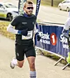 Kristian Ulriksen, deltaker med startnummer 1553 løper i Lierløpet. Han er kledd i mørkt treningstøy og sportsbriller, og passerer et område med sponsorbannere langs løypa.
