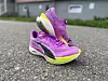 Et par løpesko fra Puma i lilla og gult står på asfalt, klare til bruk. Den lette og fargerike designen fremhever skoenes sporty preg, laget for løping og trening. Bildene understreker moderne joggesko med fokus på ytelse og komfort.