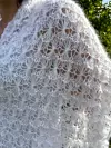 Nærbilde av et hvitt, luftig sjal i mohair med tydelig «blomster i snø»-struktur. Lyset fremhever mønsteret og den fluffy teksturen.