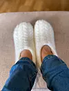 Hvite, tovede tøfler med flettemønster, fotografert på føtter med jeans.