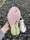 Undersiden av en løpesko med karbonplate – såle i rosa og lysegrønn gummi med slitemerker – viser karboninnlegg og mellomsåle, med grusunderlag i bakgrunnen.