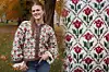 Renate-jakken i høstlig parklandskap, strikket med røde og grønne blomster på hvit bunn. Brune kanter og strukturert mønster i Peer Gynt-garn. Nærbilde viser tulipanmønster i rutearrangement.