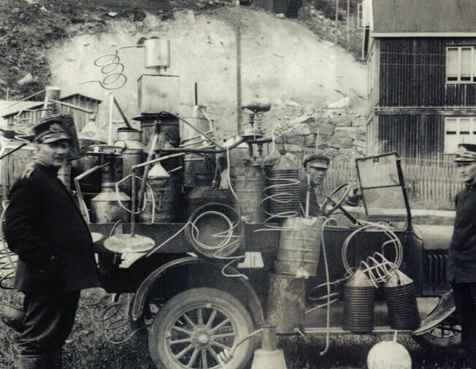 Tre politimenn med beslaglagte hjemmebrentapparater. Bildet er fra 1920. Tre politimenn med beslaglagte hjemmebrentapparater. Bildet er fra 1920. Foto: Justismuseet – Det nasjonale museet for politi, rettsvesen og kriminalomsorg