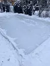 Skøytebanen i hagen på dagtid, der isen har begynt å legge seg jevnt etter flere dagers påfylling og frost.