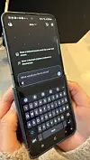 Hender som holder en smarttelefon med tastatur åpent og en KI-chat på skjermen.