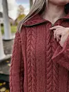 Person iført rustfarget flettestrikket genser med høy hals og glidelås utendørs.
