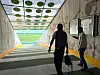 To personer går gjennom en spillertunnel mot en fotballbane i sollys.