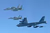 Et amerikansk B-52-bombefly eskortert av to japanske F-15-jagerfly på klar himmel.
