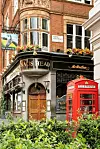 Tradisjonell London-pub med rød telefonkiosk og blomsterdekor i en smal gate.