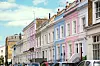Rekke pastellfargede byhus i London med parkerte biler foran.