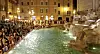 Stor folkemengde rundt en opplyst fontene i Roma om kvelden.