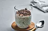 Glass med chia-pudding toppet med sjokoladeflak ved siden av en skje på bordet.