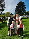 Familie i tradisjonelle klær står sammen på en grønn plen en solrik dag.