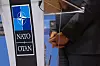 Nato-logo ved talerstol og en dresskledd persons foldede hender under presseuttalelse.